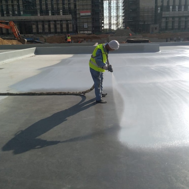 A close-up view of a spray gun emitting a fine mist of polyurea waterproofing material onto a rough concrete surface.
