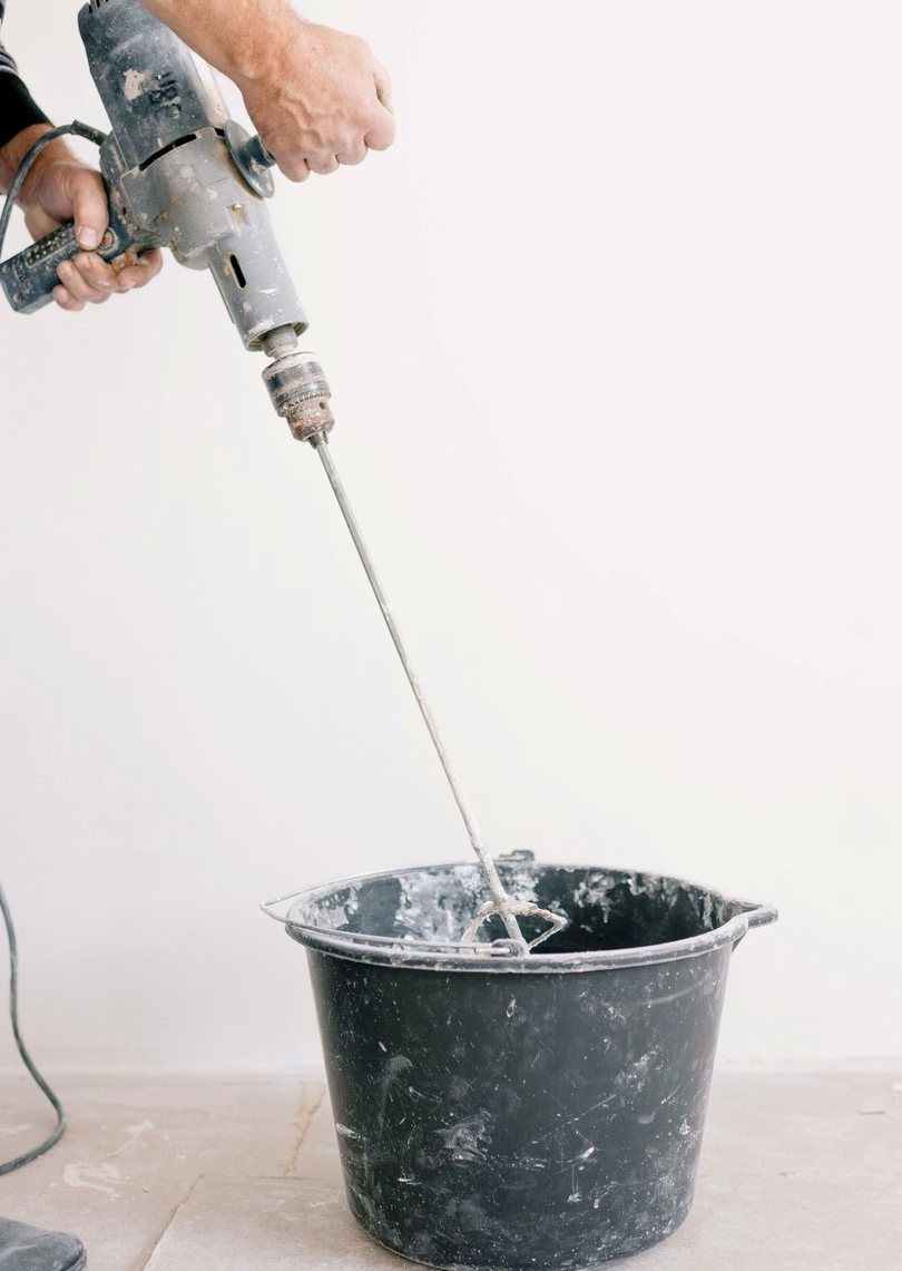 Mixing cementitious bathroom waterproofing components in a bucket with an electric drill and paddle