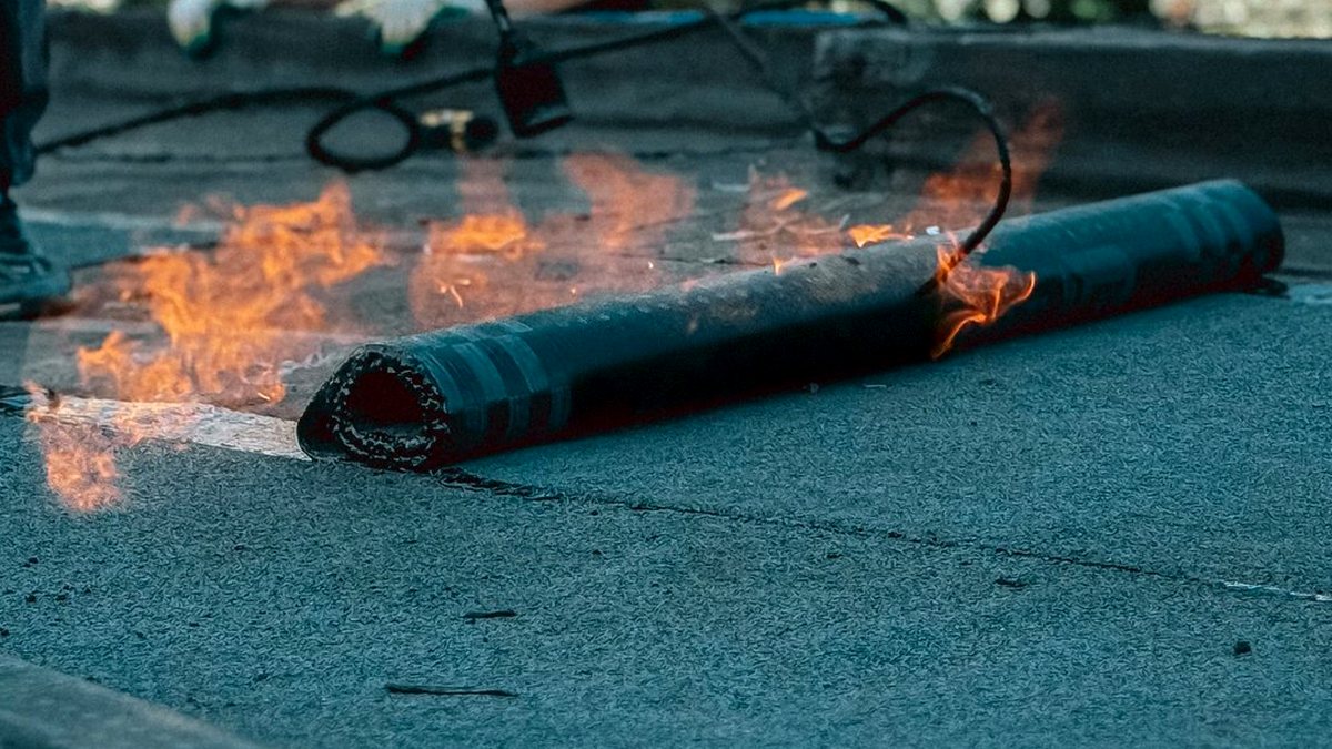 Bitumen waterproofing membranes being torch-applied as the roll is unrolled on a flat roof
