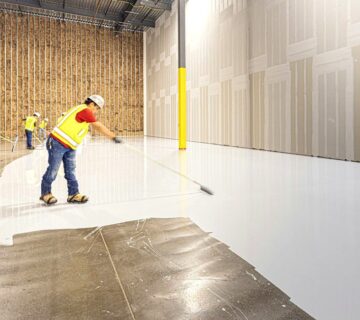 Crew spreading an epoxy flooring coat over a warehouse concrete slab with long-handled rollers