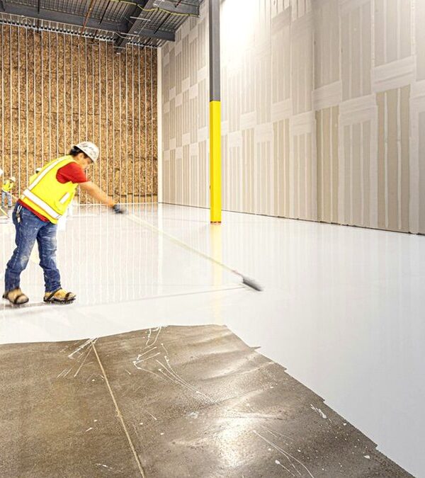 Crew spreading an epoxy flooring coat over a warehouse concrete slab with long-handled rollers