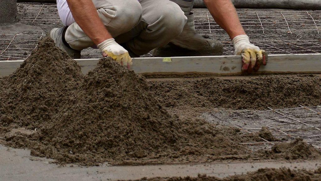 Screed work affects polyurea roof waterproofing cost: worker levelling a sand-cement screed to falls with a straightedge on a concrete roof slab
