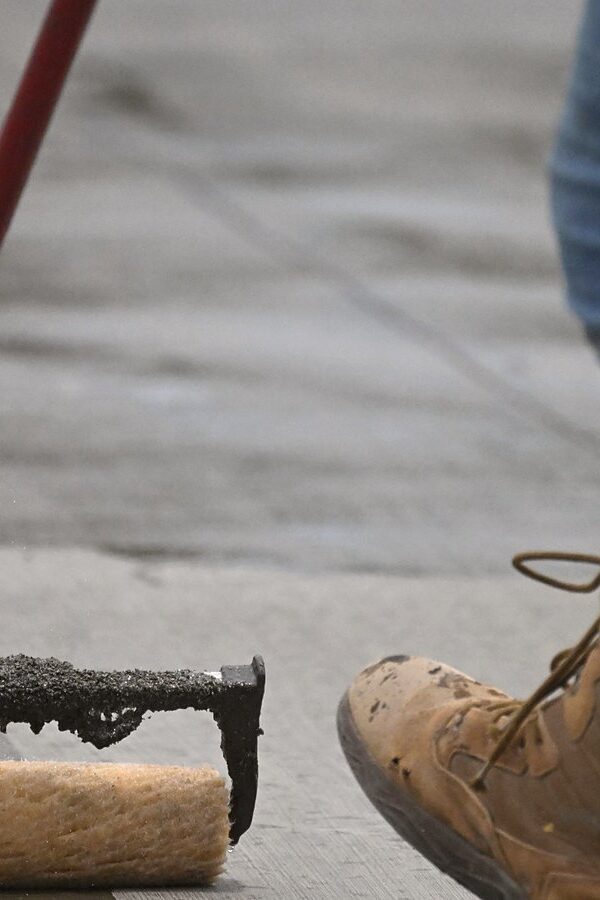 Worker spreading a liquid coat with a squeegee followed by a roller, the same way polyurea primer is spread on concrete