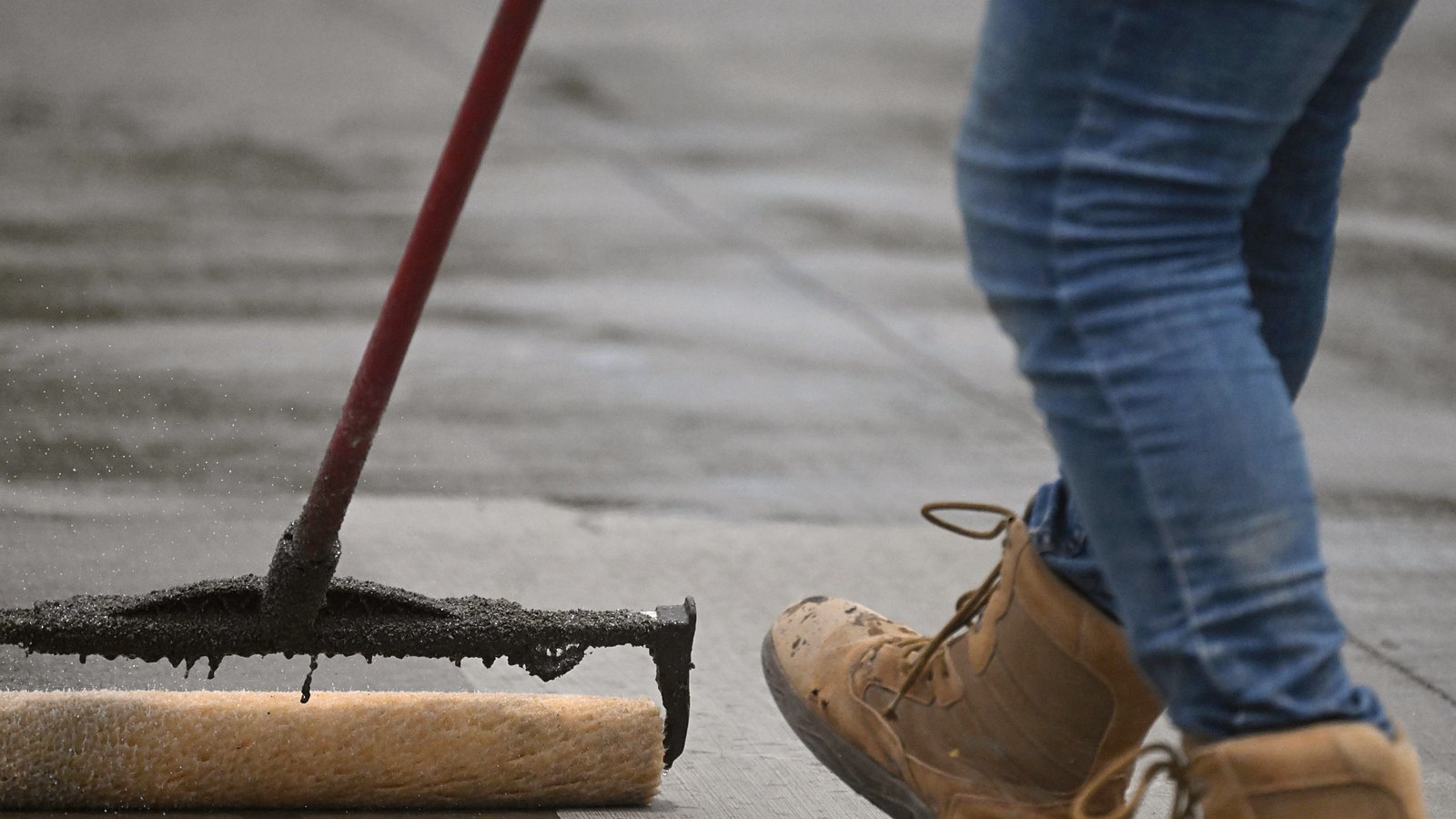 Worker spreading a liquid coat with a squeegee followed by a roller, the same way polyurea primer is spread on concrete
