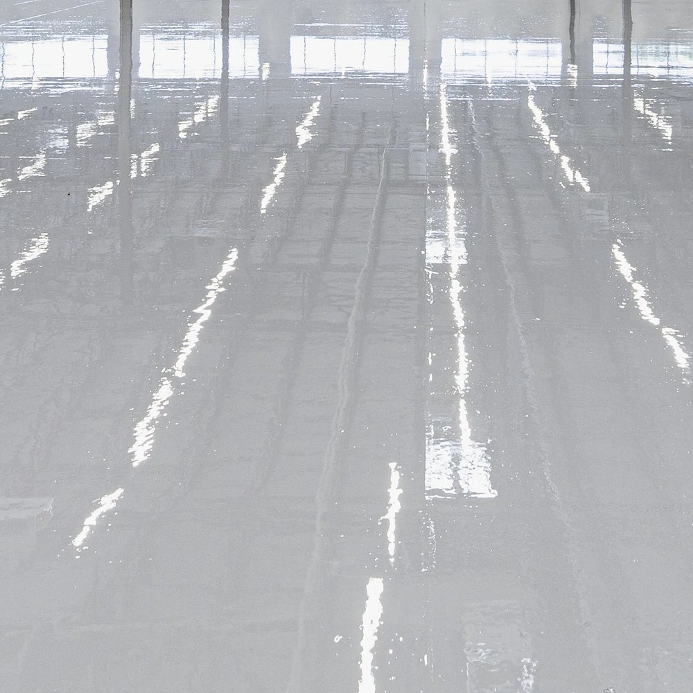 Freshly applied polyurea primer giving a smooth, glossy wet-look finish on a light-grey concrete floor
