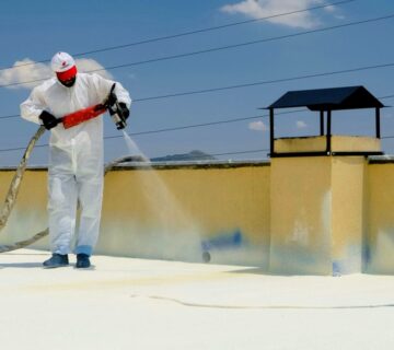 Applicator in a protective suit spraying spray foam roof insulation onto a flat concrete roof with a plural-component gun