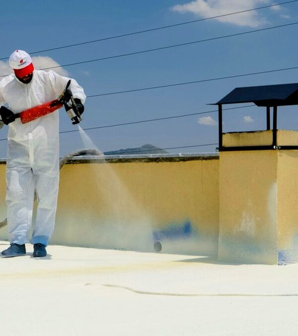 Applicator in a protective suit spraying spray foam roof insulation onto a flat concrete roof with a plural-component gun