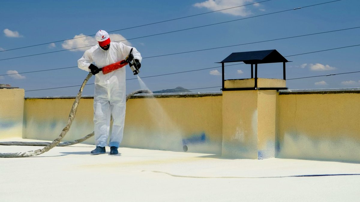 Applicator in a protective suit spraying spray foam roof insulation onto a flat concrete roof with a plural-component gun